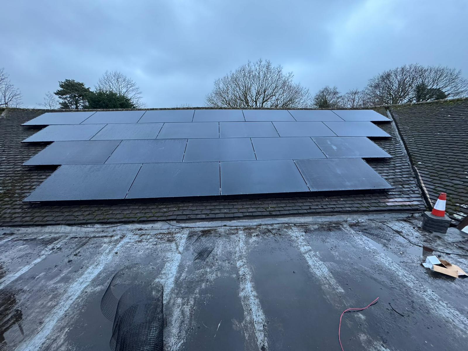 All-black solar panels fitted on a tiled roof slope, seen from an adjoining flat roof.