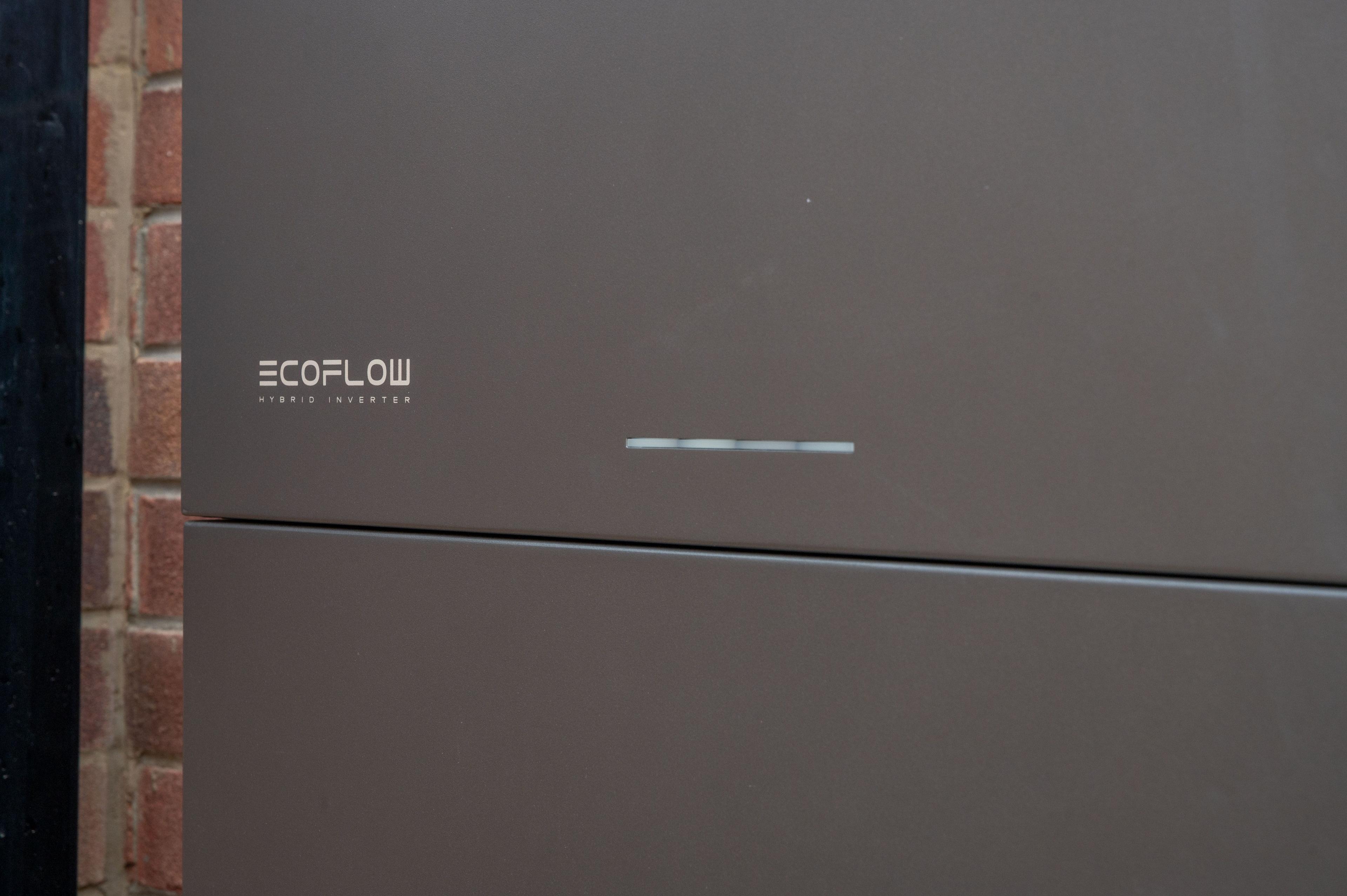 Close-up of the front panel of an EcoFlow hybrid inverter mounted against a brick wall.