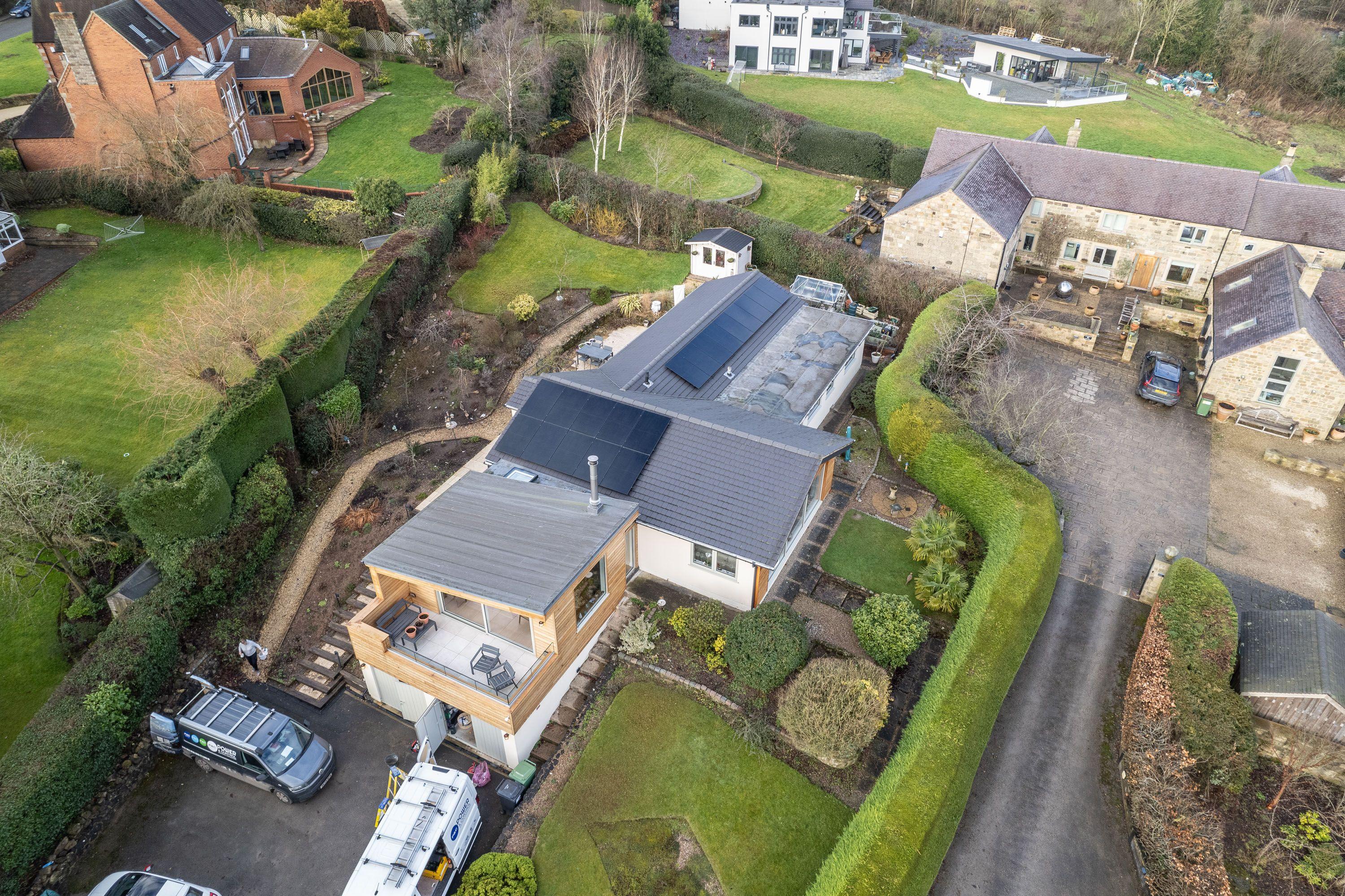 Aerial view of black solar panels on two roof sections of a bungalow, with vans parked on the drive.