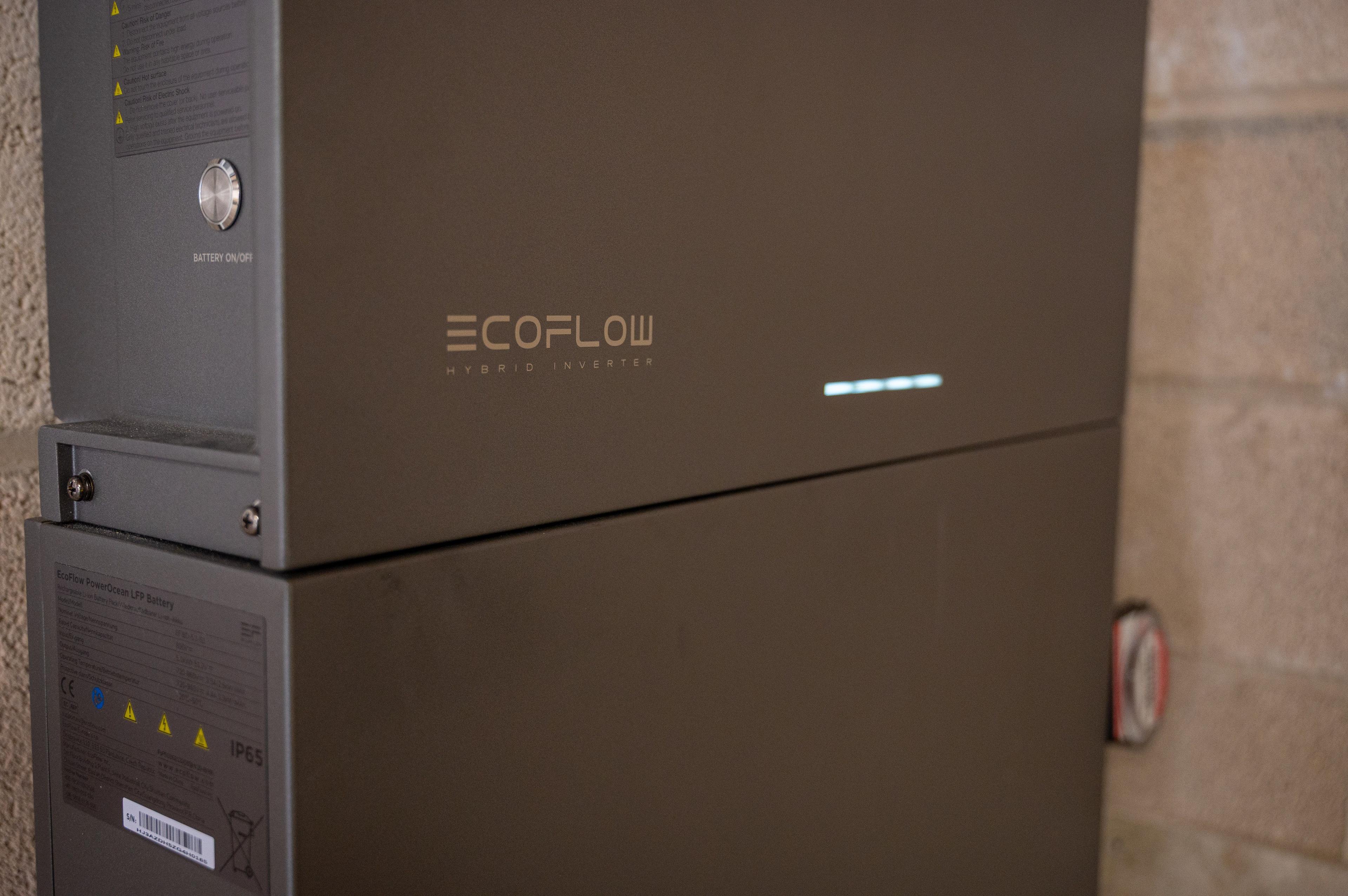 Close-up of an EcoFlow hybrid inverter stacked on a battery module against a block wall.