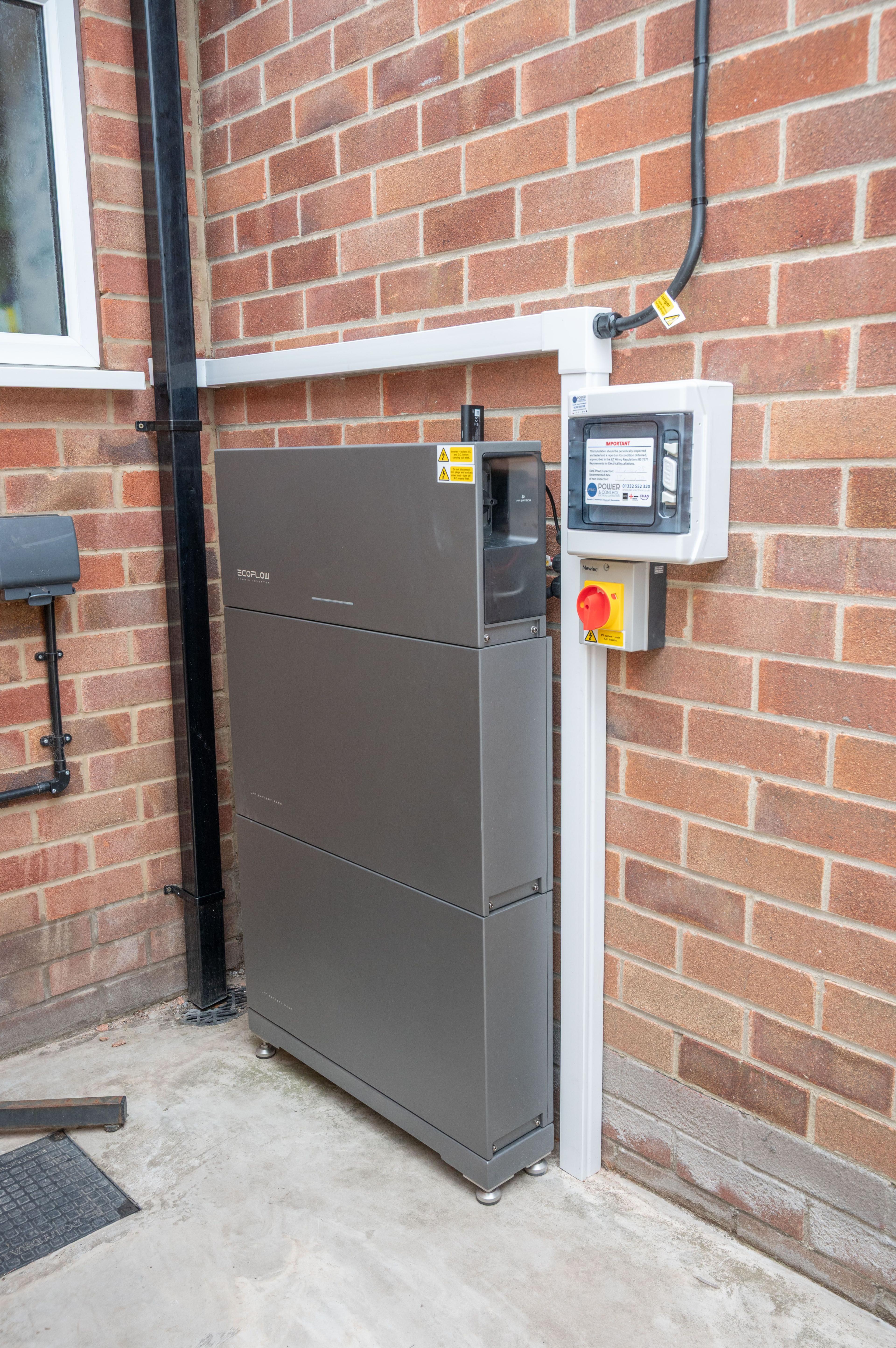 EcoFlow battery and inverter stack beside an isolator and enclosure on the outside wall of a house.