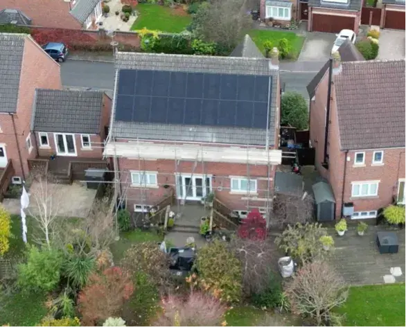 Aerial view of black solar panels across the rear roof of a red-brick house, with scaffolding still in place.