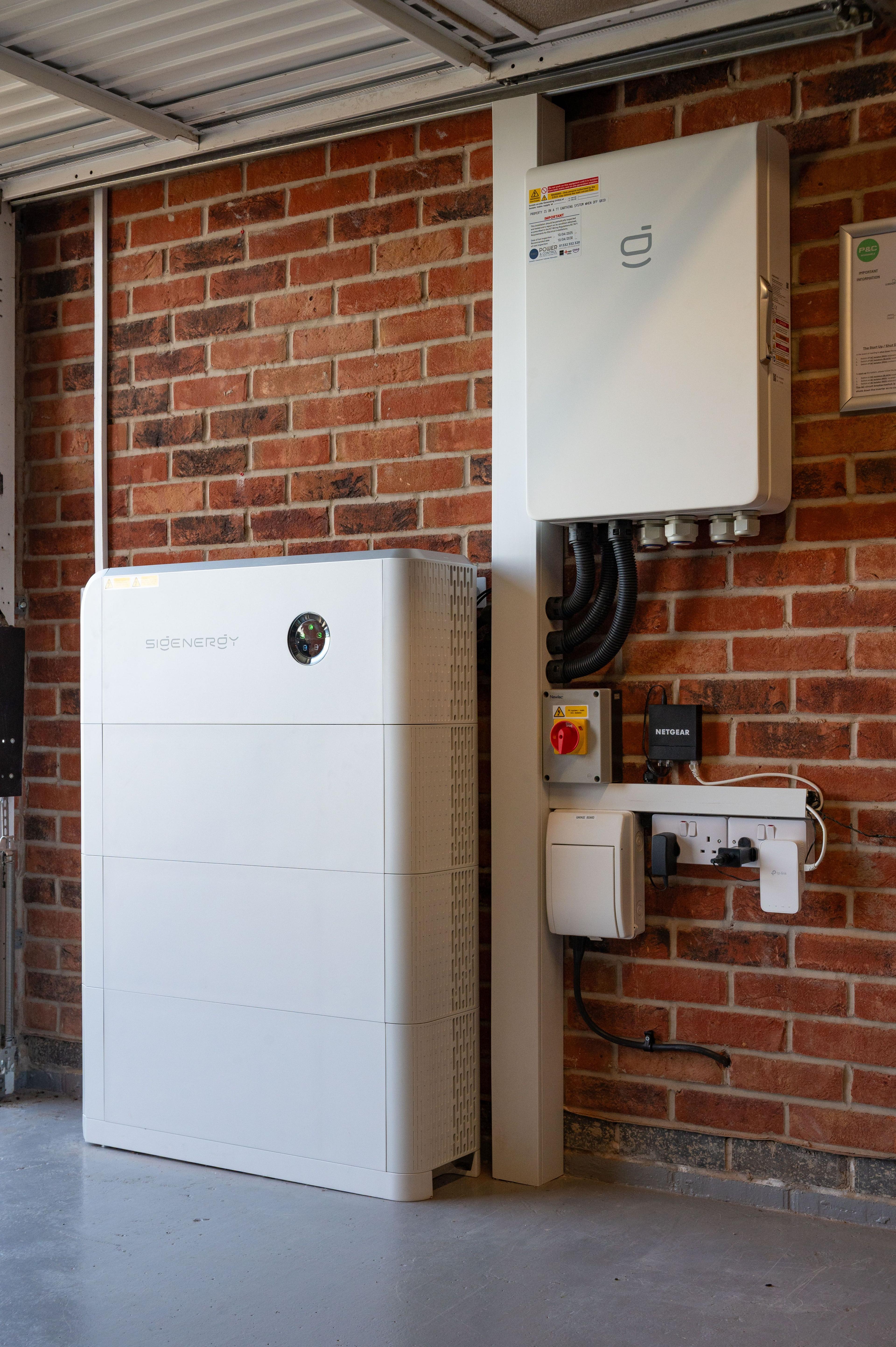 Sigenergy battery stack and a wall-mounted inverter with isolator and cabling in a garage.