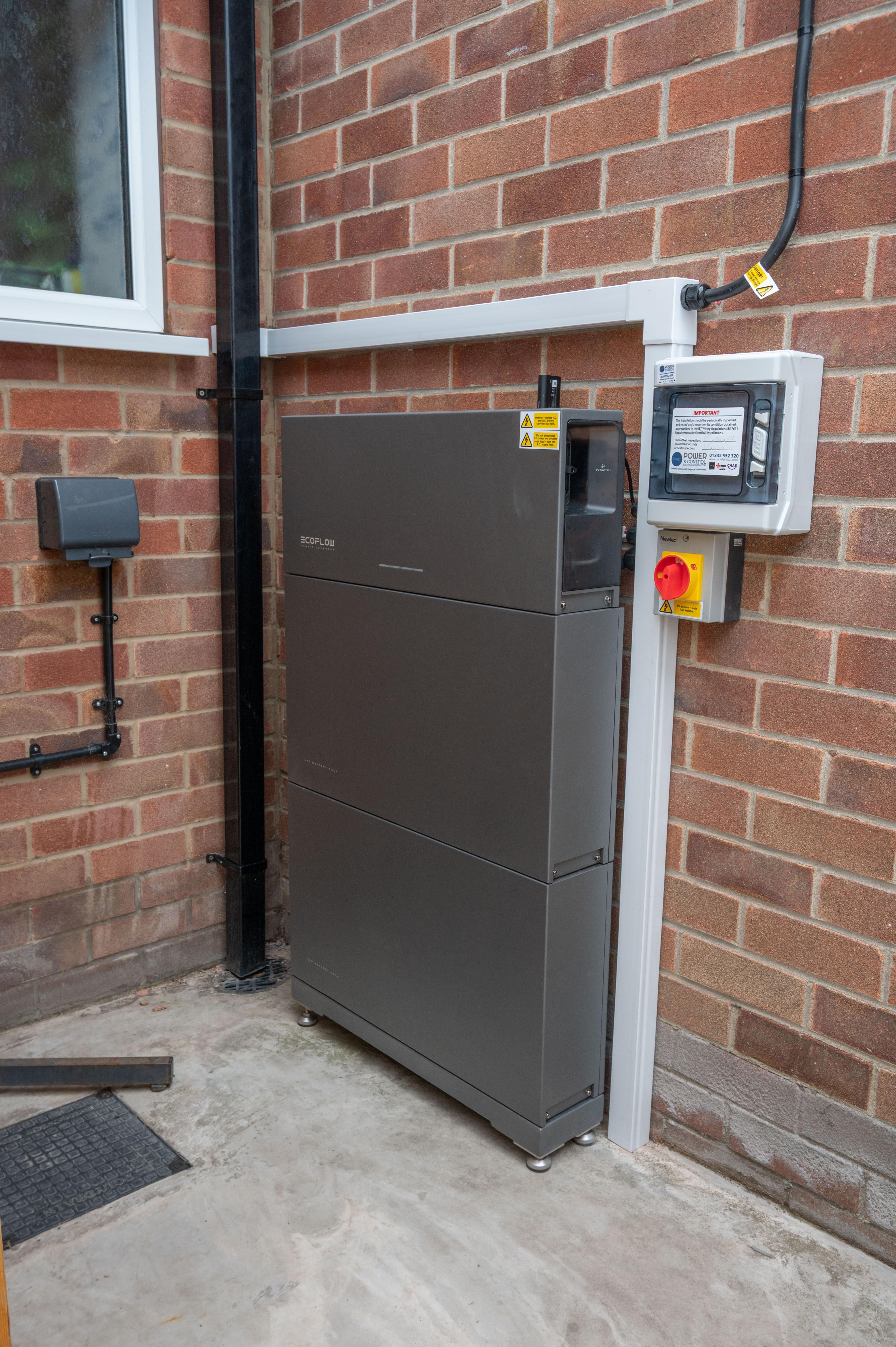 EcoFlow battery stack with an isolator and enclosure, installed against a brick wall outside a house.