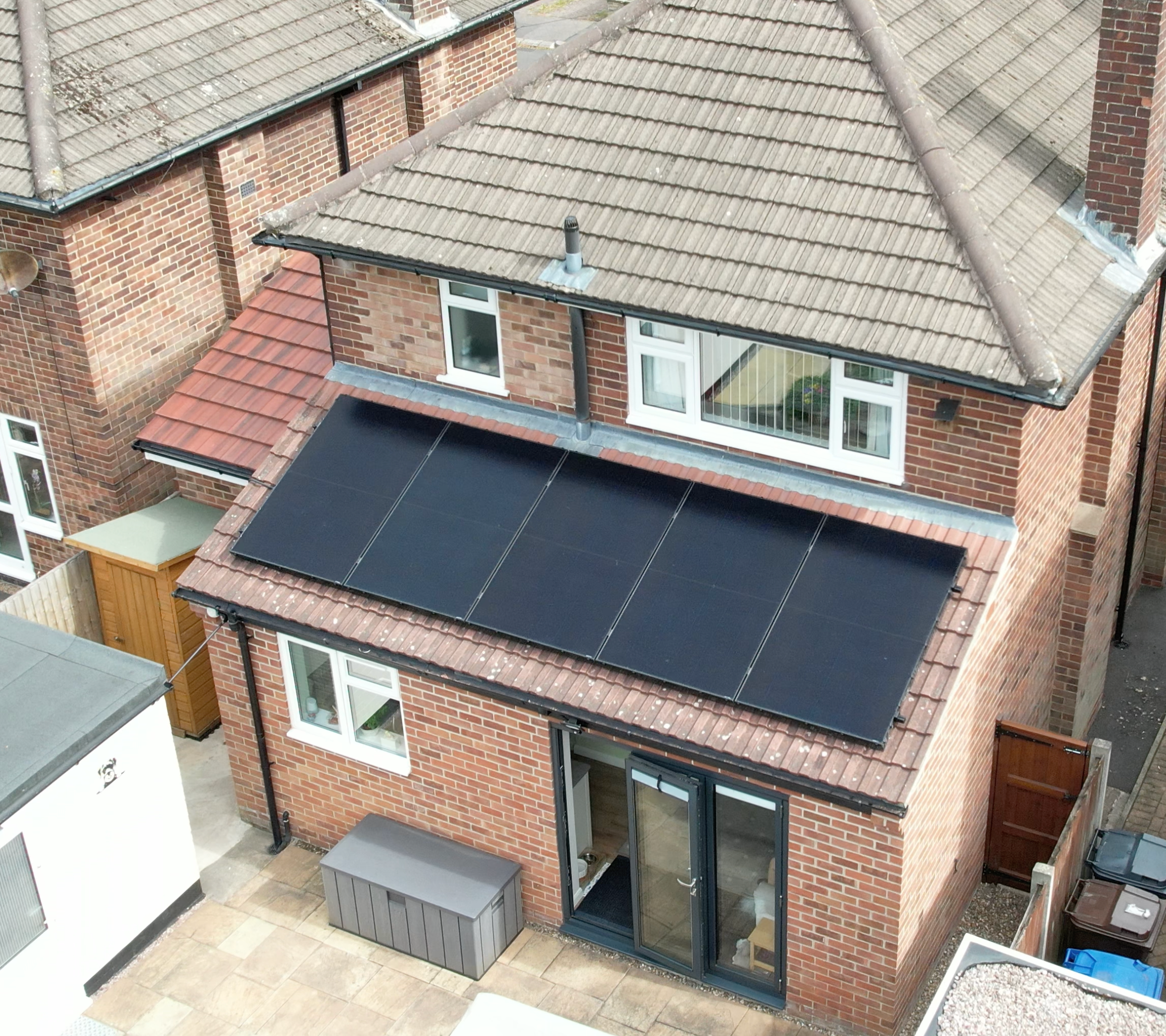 Aerial view of a brick semi-detached house with a row of black solar panels on a rear single-storey roof.