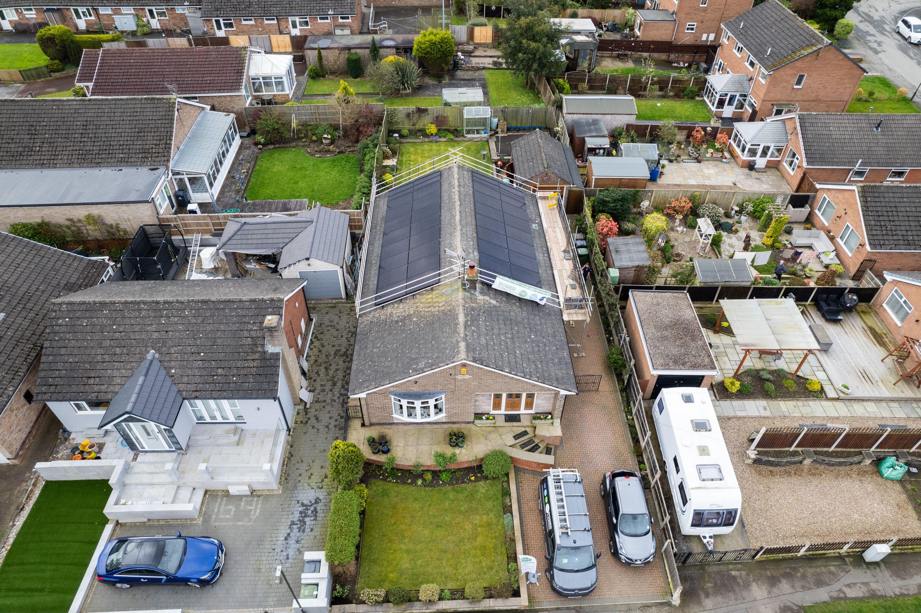Aerial view of black solar panels on a bungalow roof, with edge protection around the roof.