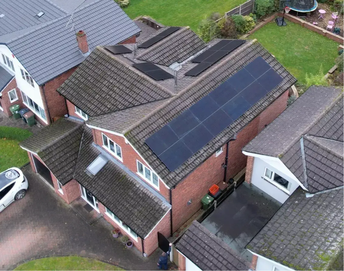 Aerial view of black solar panels on several roof slopes of a red-brick detached house.