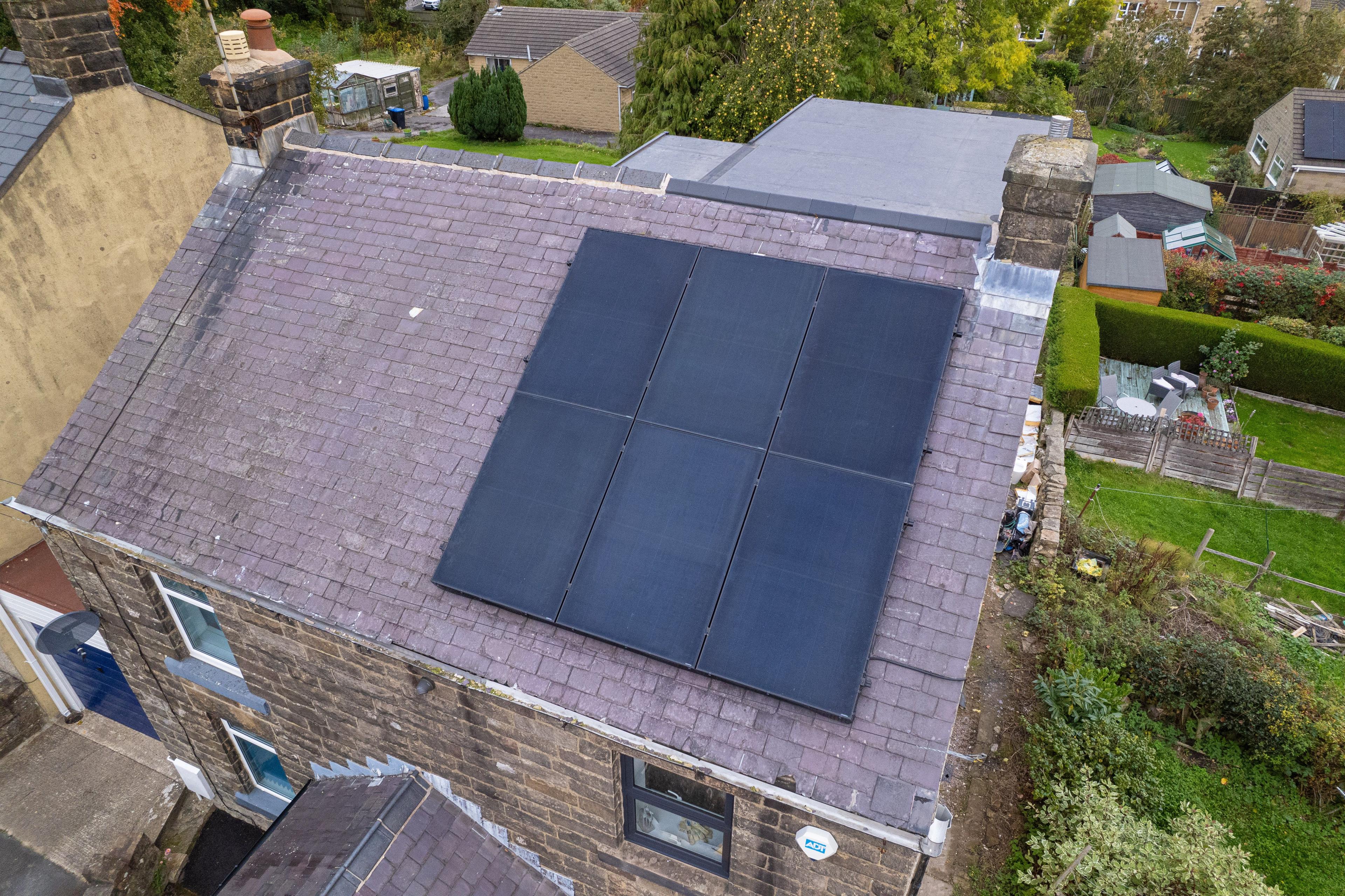 Aerial view of six black solar panels on the slate roof of a stone-built house.