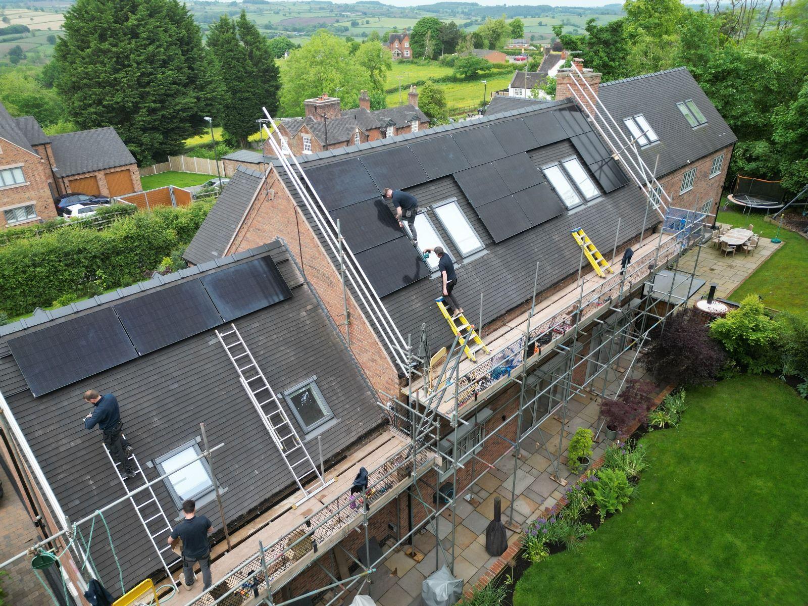 Installers on scaffolding fitting black in-roof solar panels around roof windows on a large house.