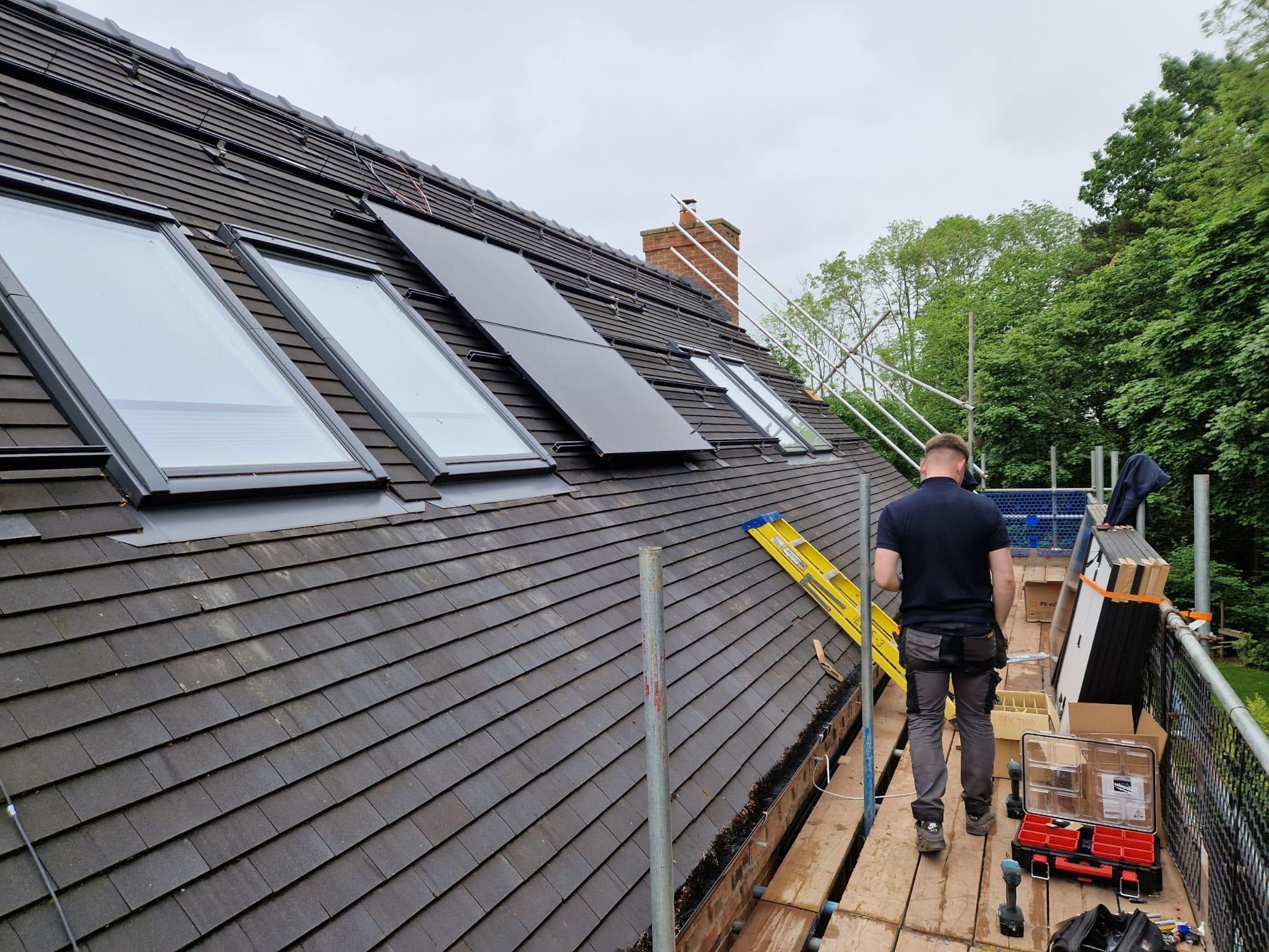 Installer on scaffolding beside black in-roof solar panels being fitted between roof windows.