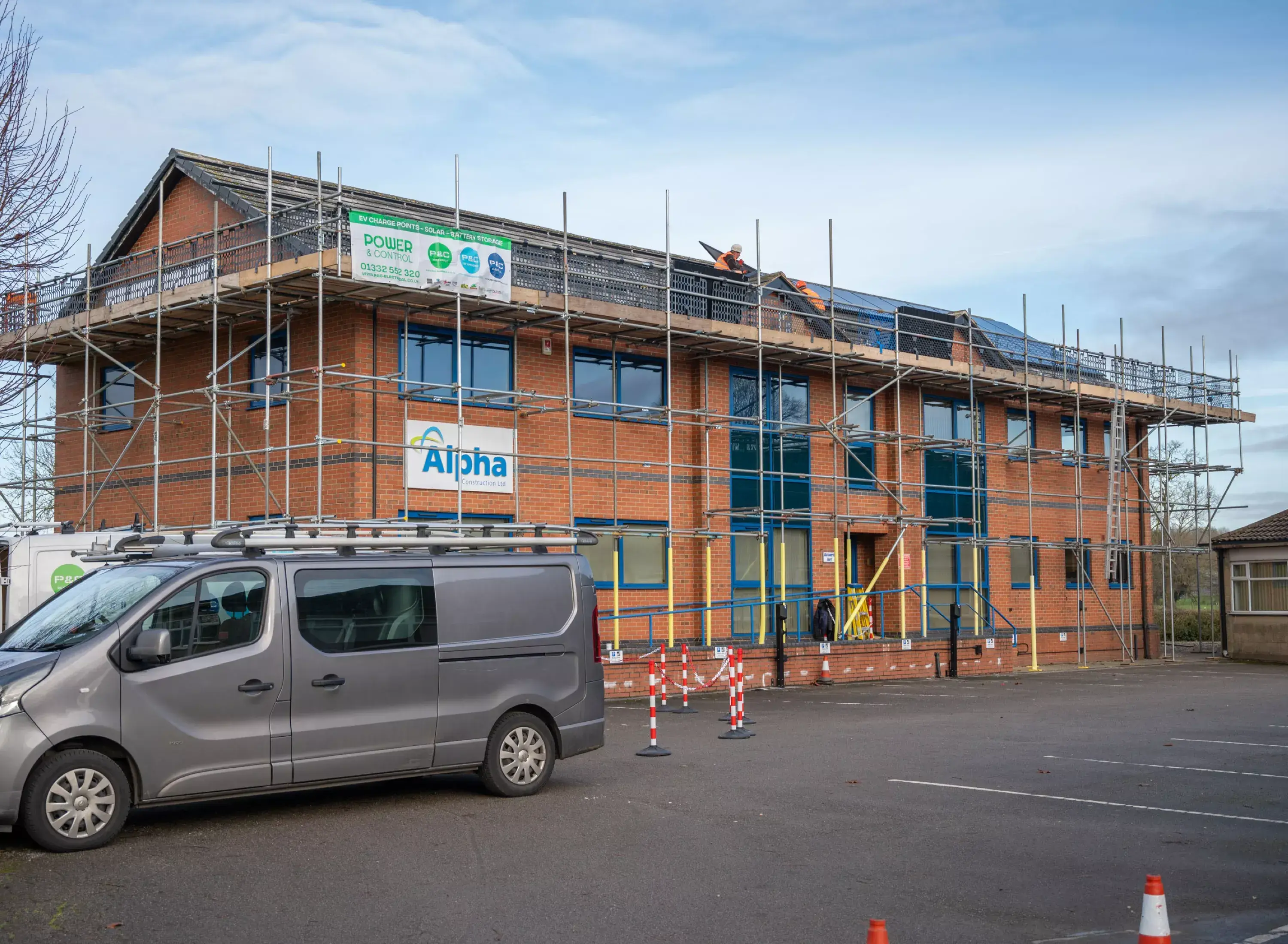 Scaffolded two-storey brick office building with installers fitting solar panels on the roof.
