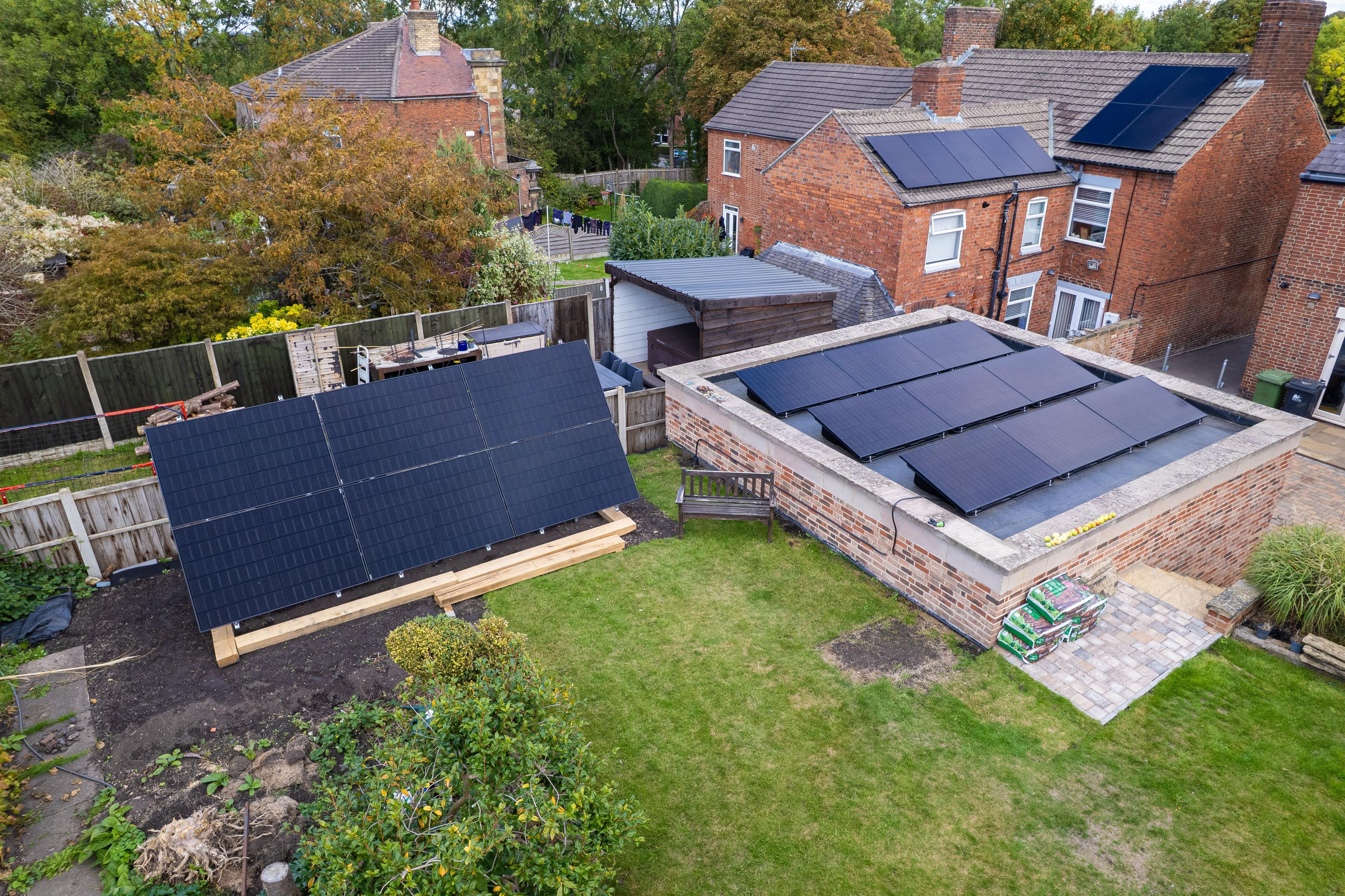 Aerial view of a garden with a ground-mounted solar array and panels on a flat garage roof.
