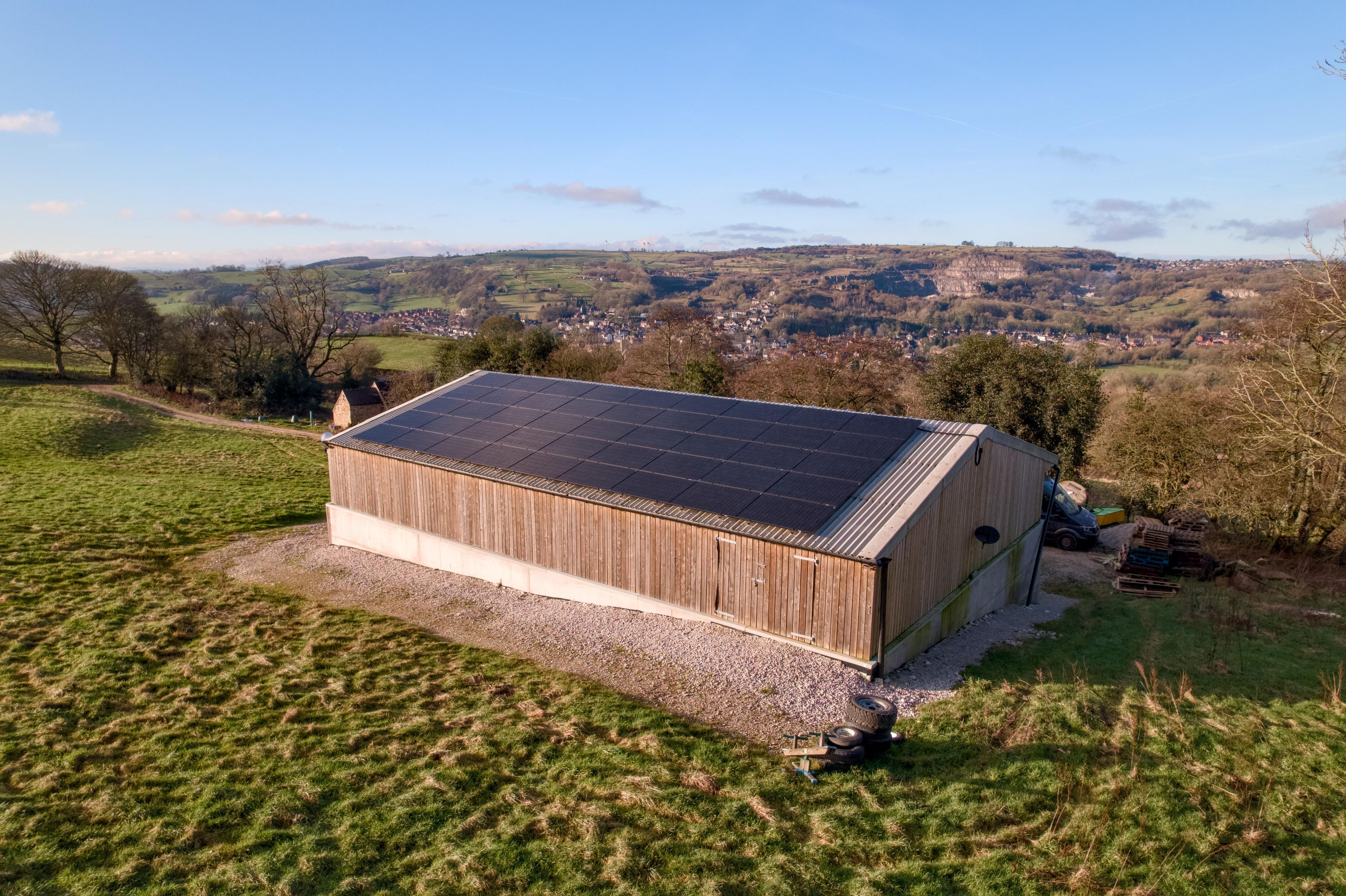 Agricultural timber-clad barn with a roof full of solar panels in hilly countryside.