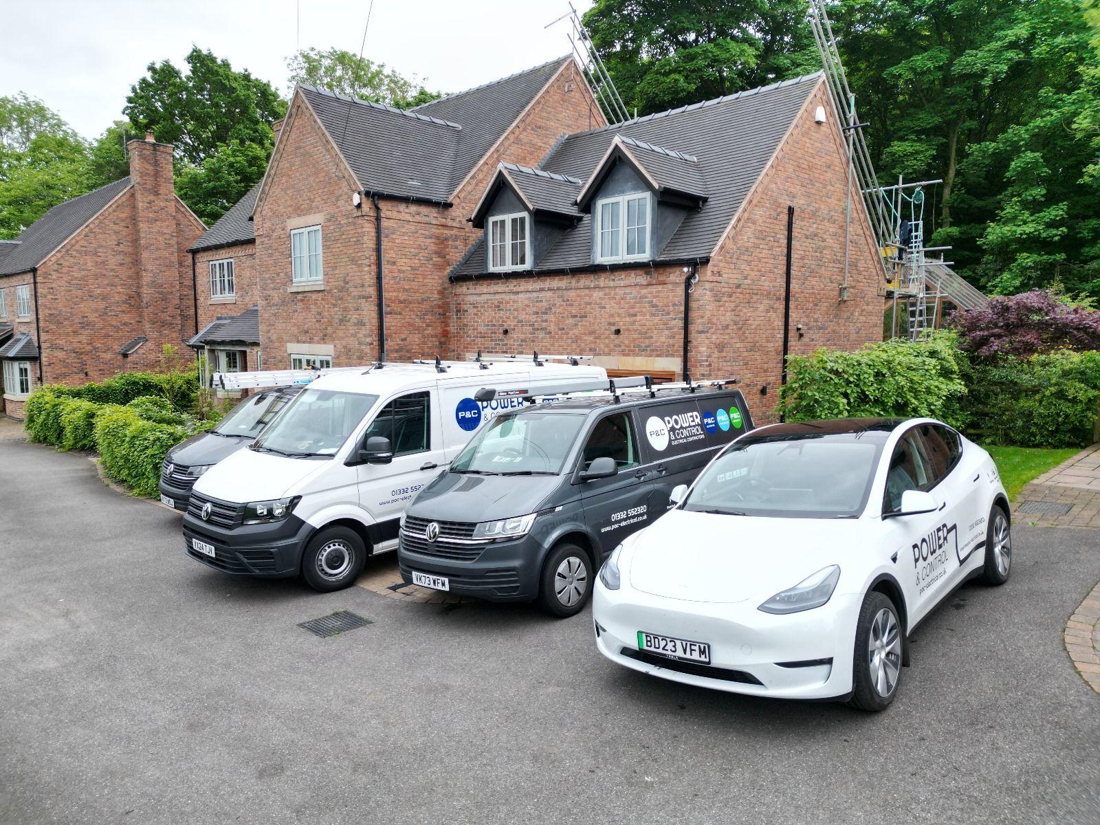 Power and Control branded vans and a branded electric car parked outside a brick house with scaffolding.