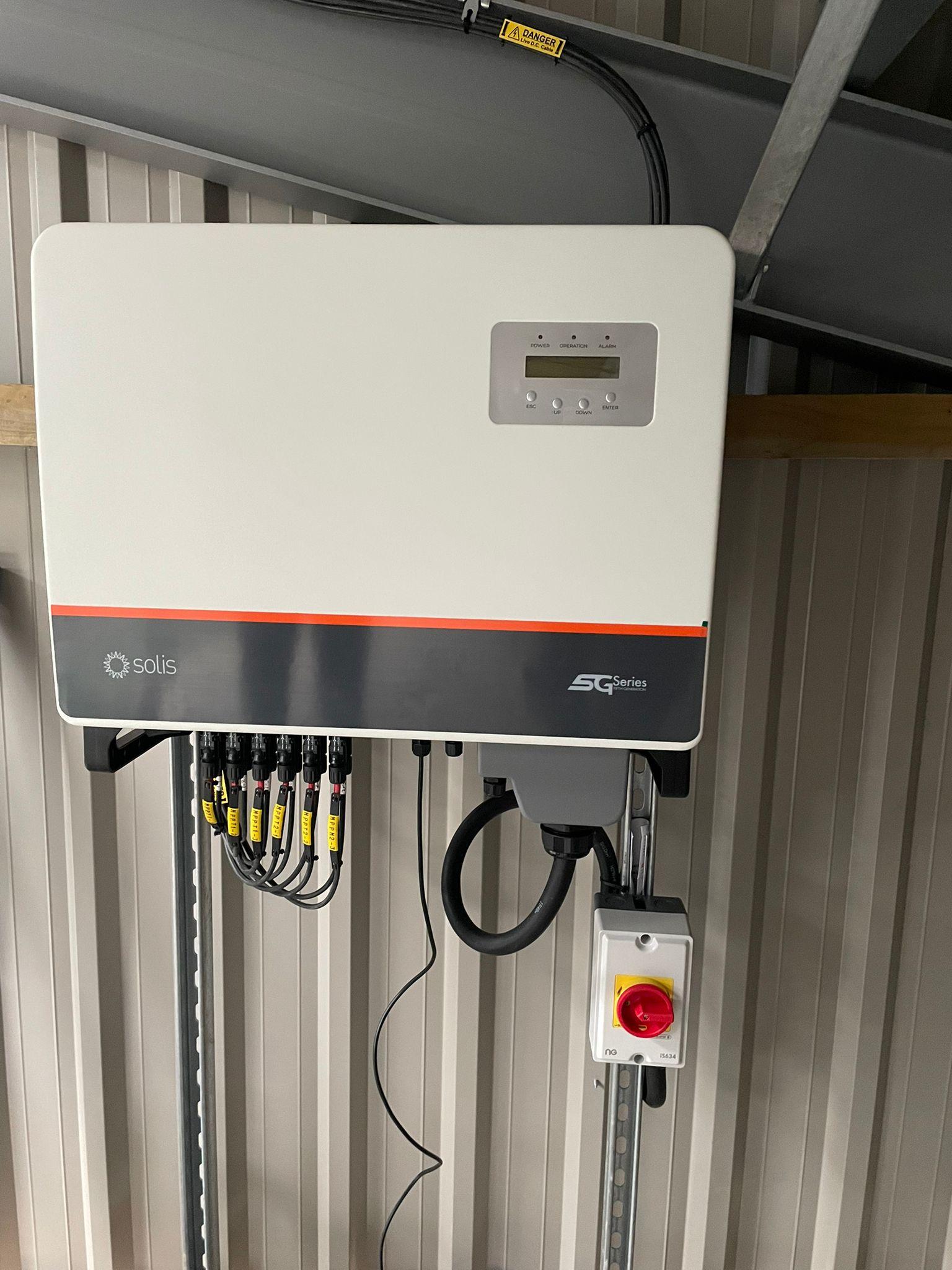A Solis inverter mounted on a barn wall with labelled DC string cables and a red and yellow isolator below.