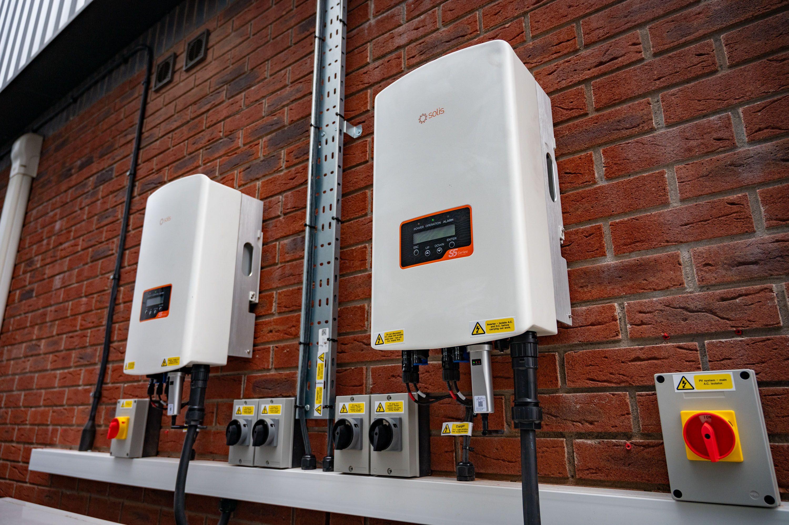 Two Solis inverters with DC and AC isolators mounted on a brick wall at a commercial site.