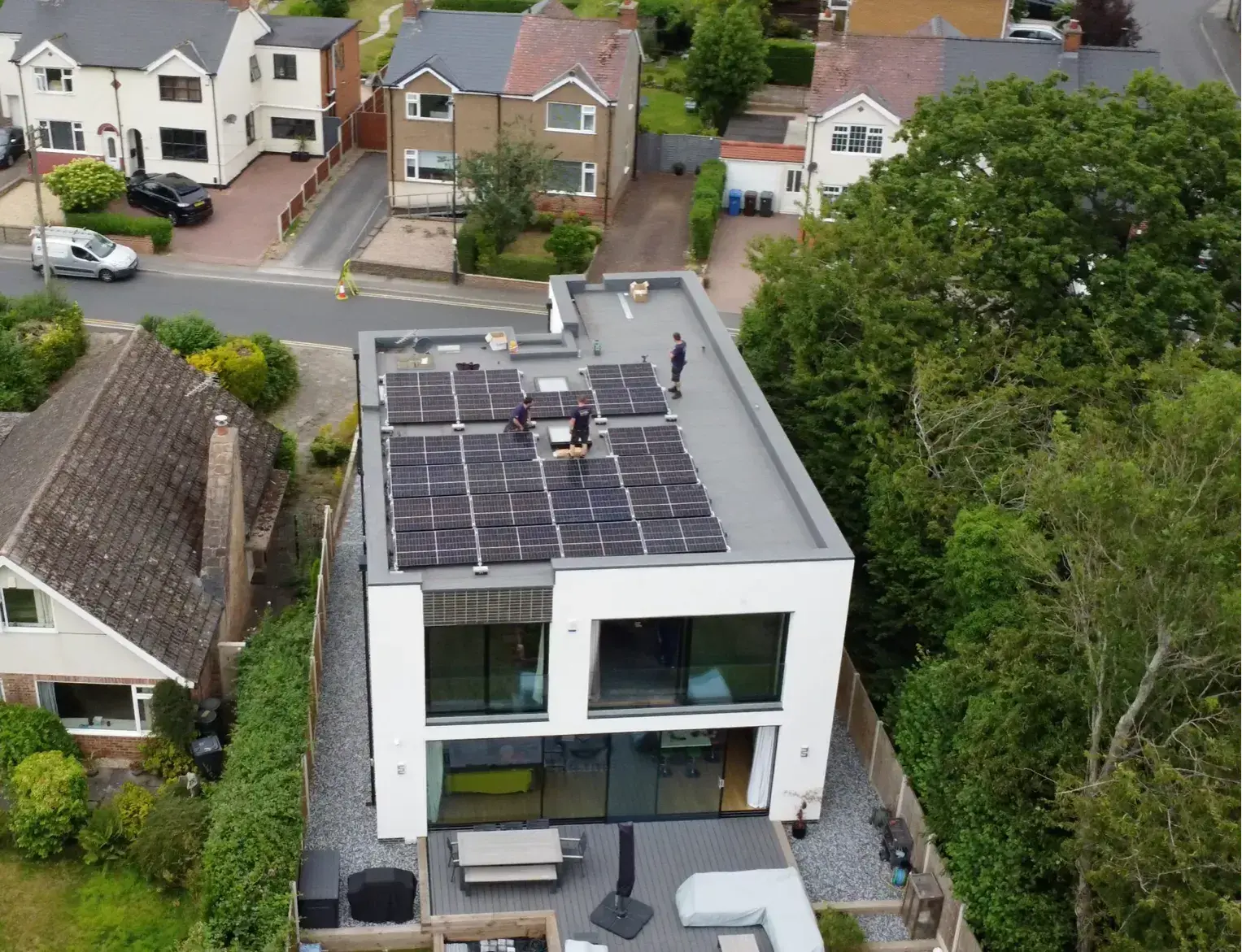 Aerial view of installers fitting solar panels on the flat roof of a modern white house.