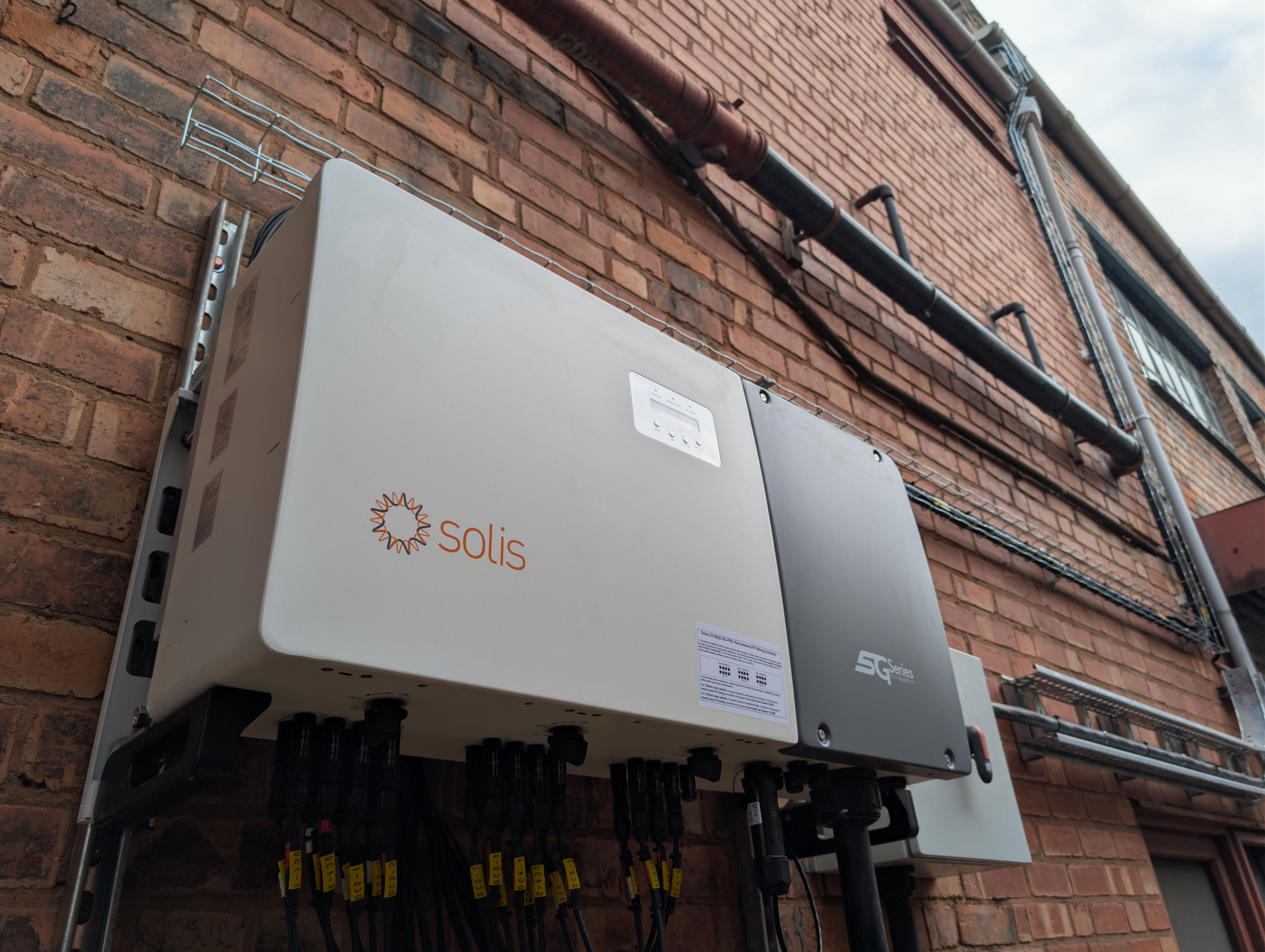 Large Solis inverter with DC string connectors mounted on a brick commercial building wall.