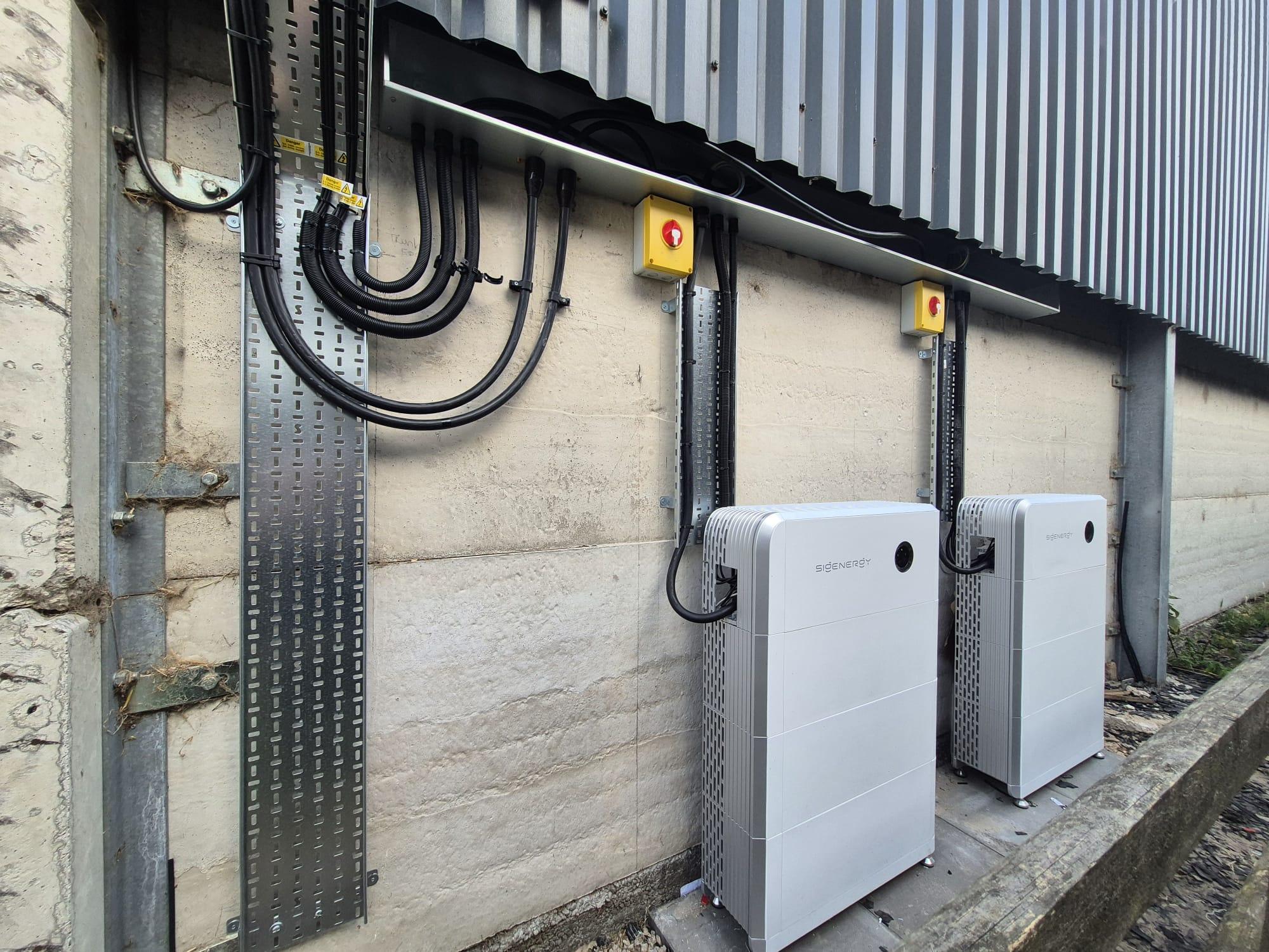 Two Sigenergy battery units with yellow isolators and cable tray on the outside wall of a commercial building.