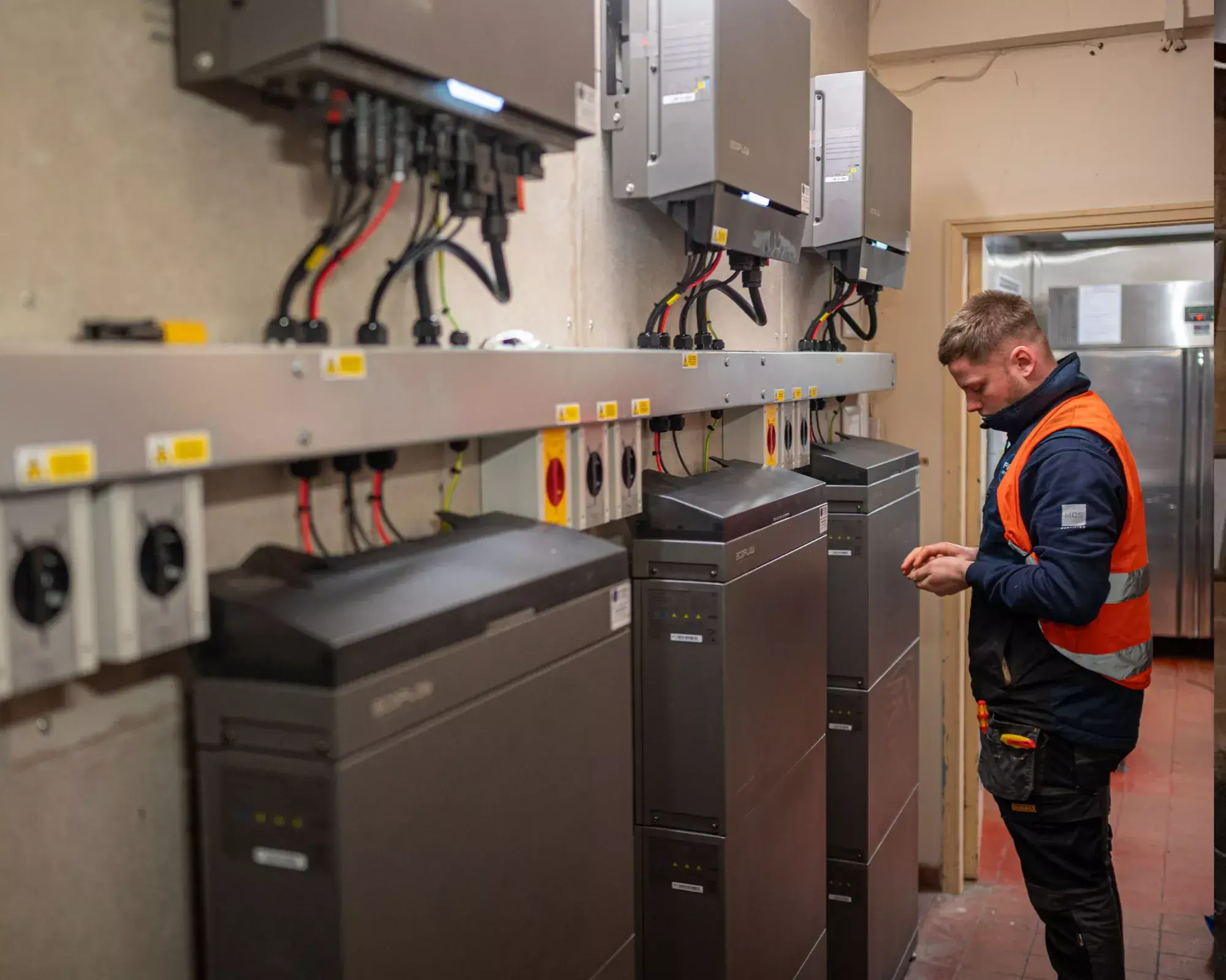 Engineer working beside a row of battery stacks and wall-mounted inverters in a plant room.