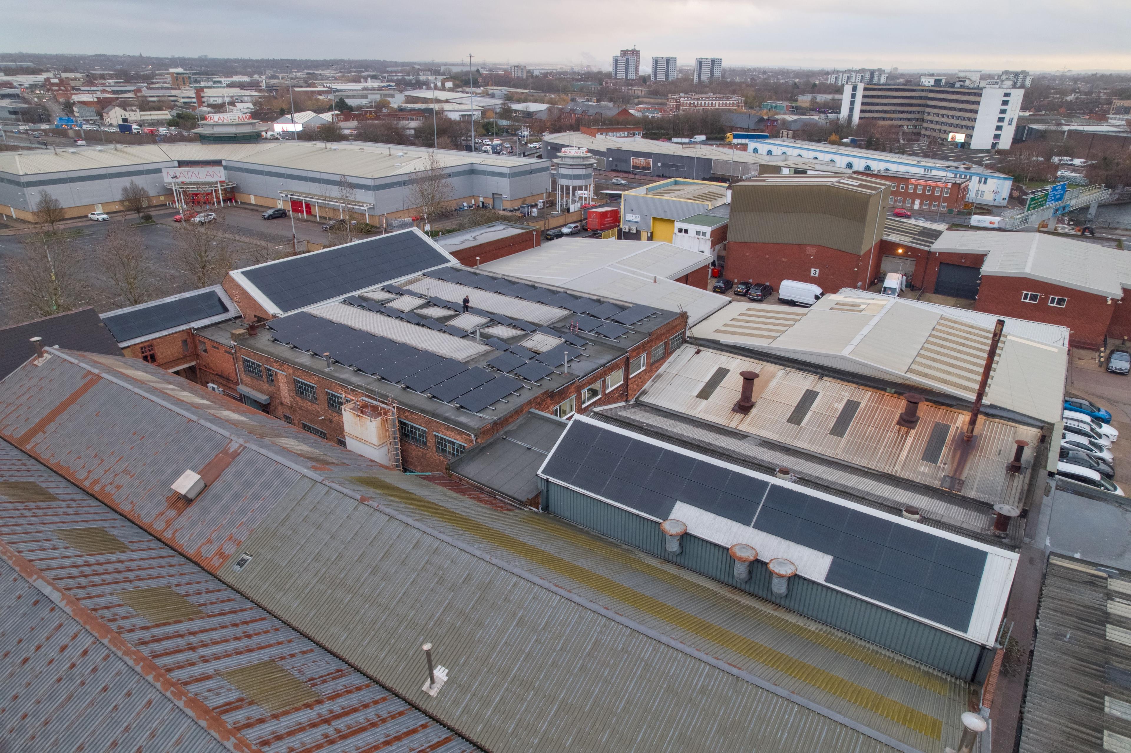 Aerial view of industrial buildings with solar panels installed across several pitched and flat roofs.