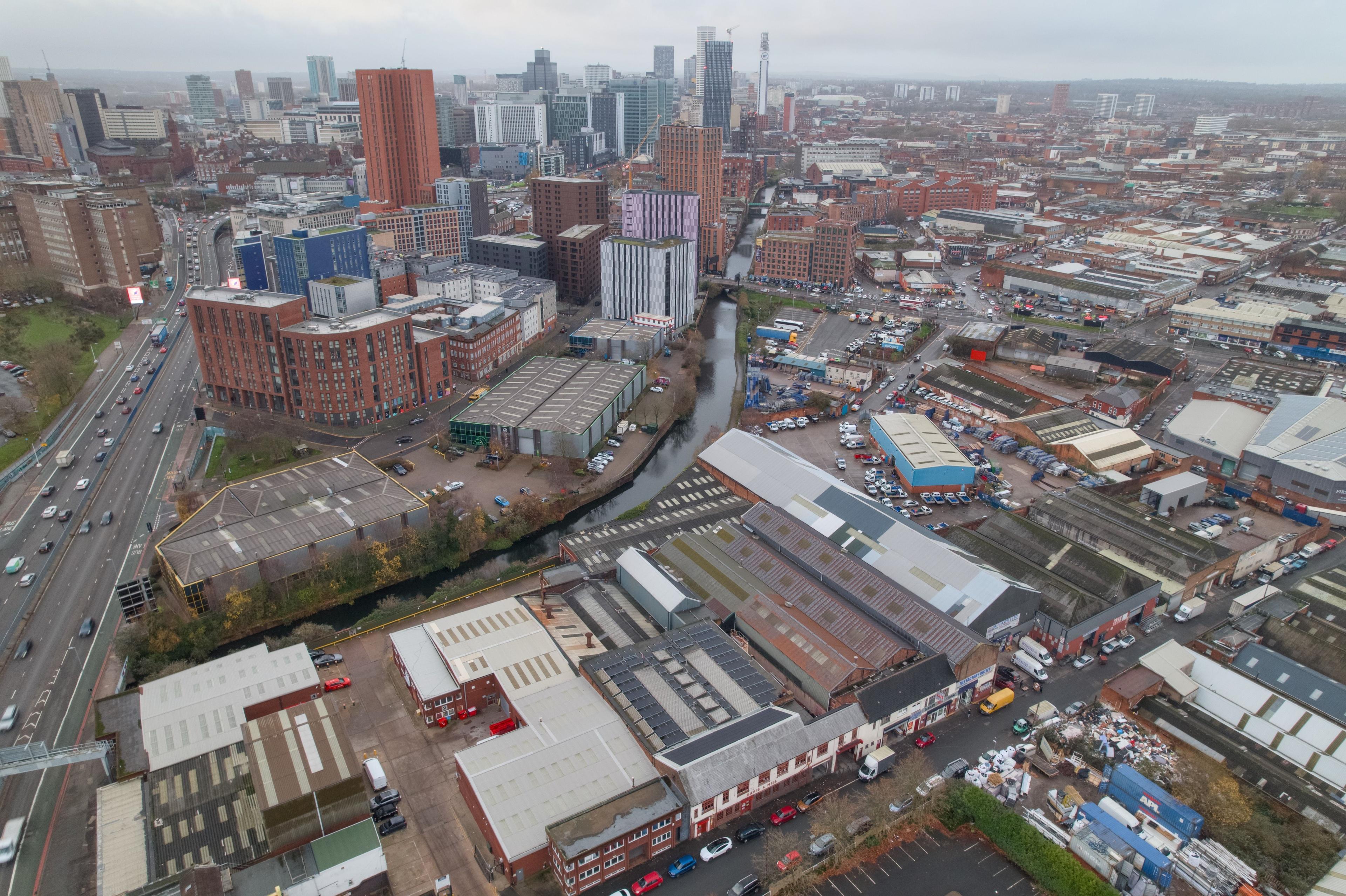 Aerial view over a city industrial estate with solar panels on several factory roofs and tower blocks behind.