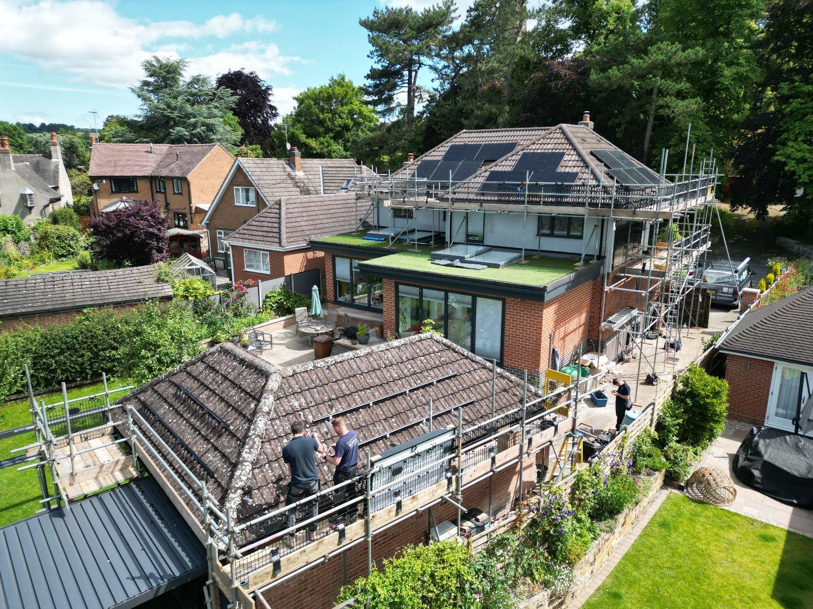 Aerial view of a scaffolded house in Breadsall, Derby, with solar panels on the roof and engineers on a garage roof.