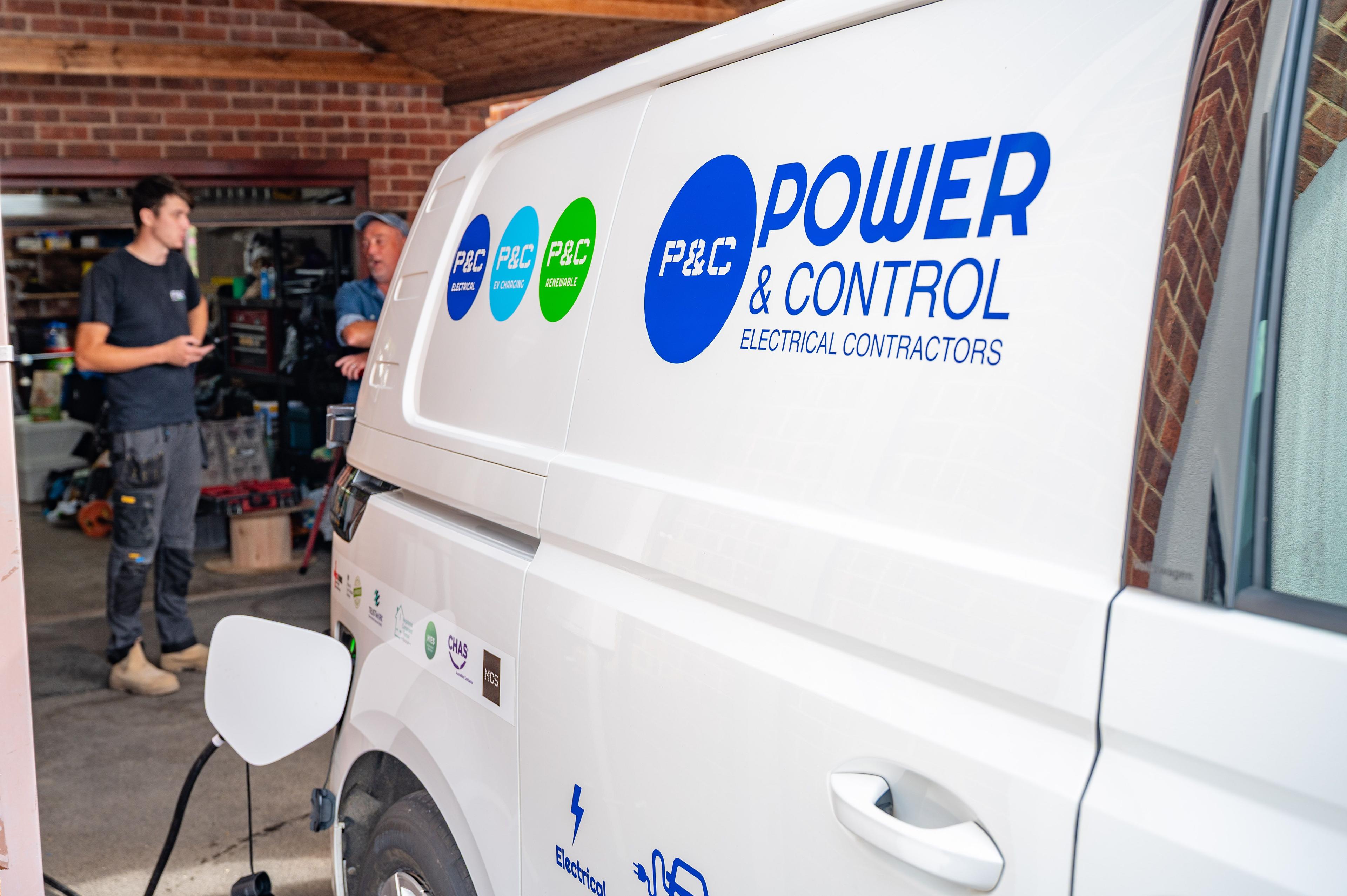 Power and Control branded van plugged in to charge, with two people talking in a garage behind.