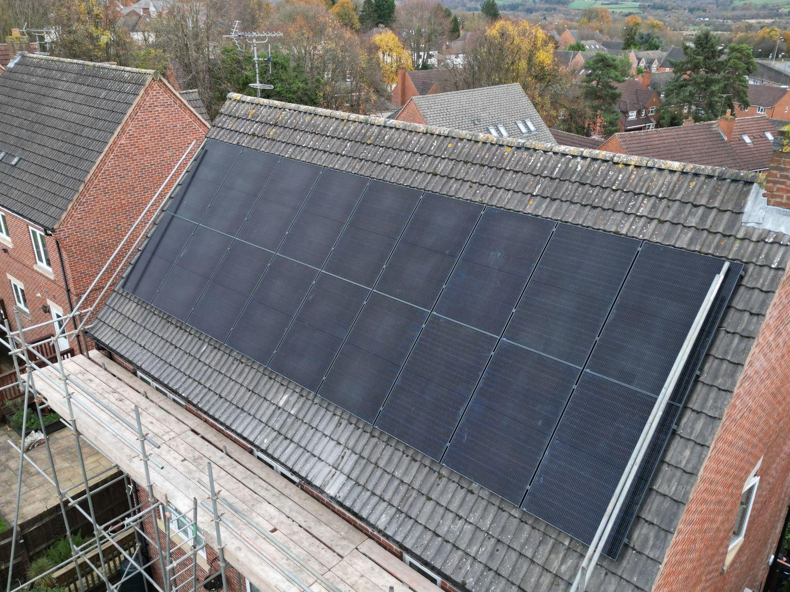 Aerial view of all-black solar panels on a tiled house roof with scaffolding along one side.